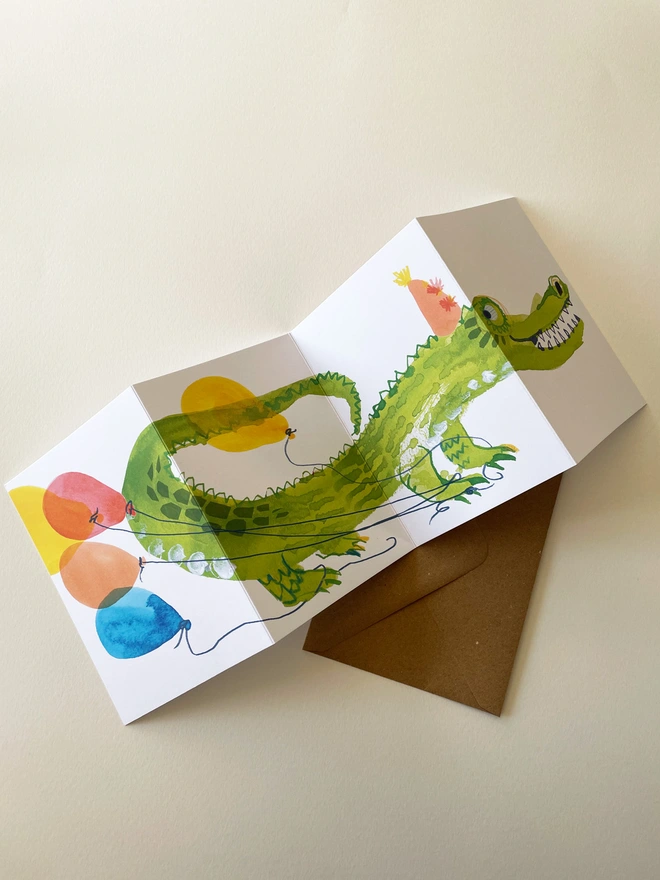Esther Kent illustrated concertina greeting card showing a creen crocodile on a white background, with colourful balloons