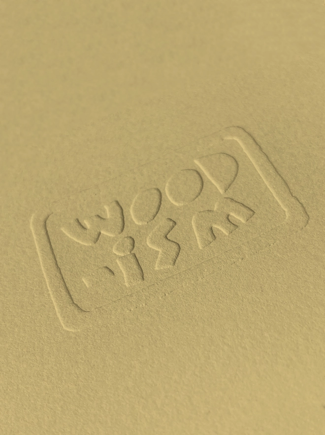A close up of the Woodism logo embossed on the corner of the yellow print