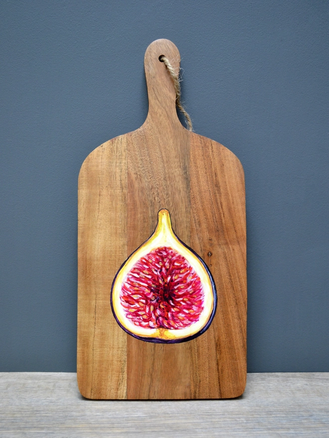 A wooden serving board with a handpainted design of a ripe fig
