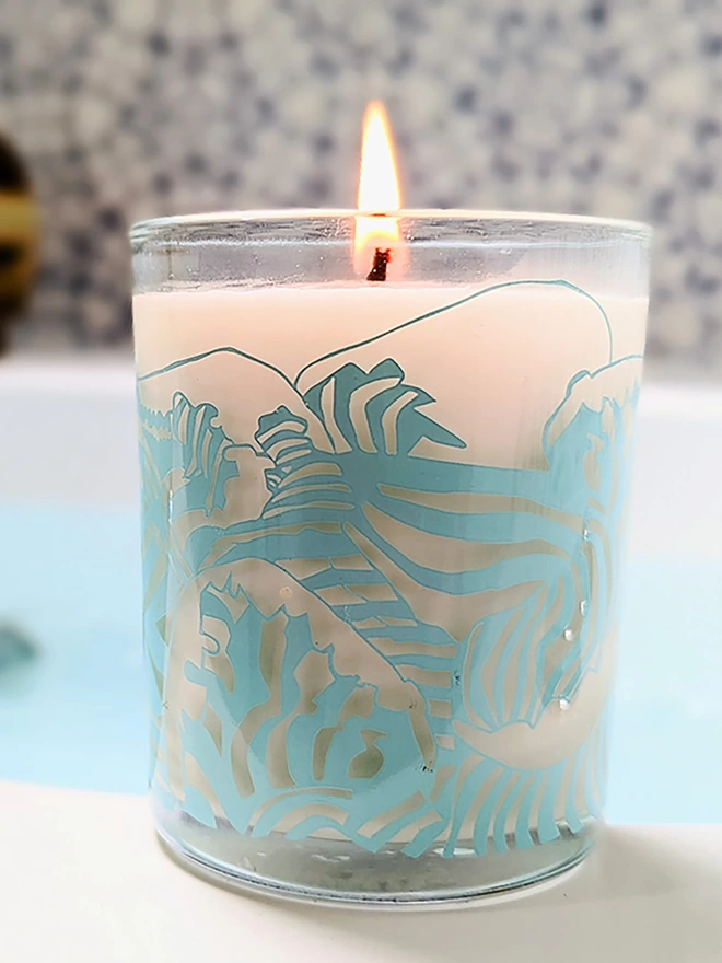 the wave black pomegranate charity candle in a reusable glass with light blue illustrations