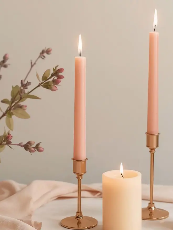 lifestyle image of peach dinner candles in brass candle holders on a table