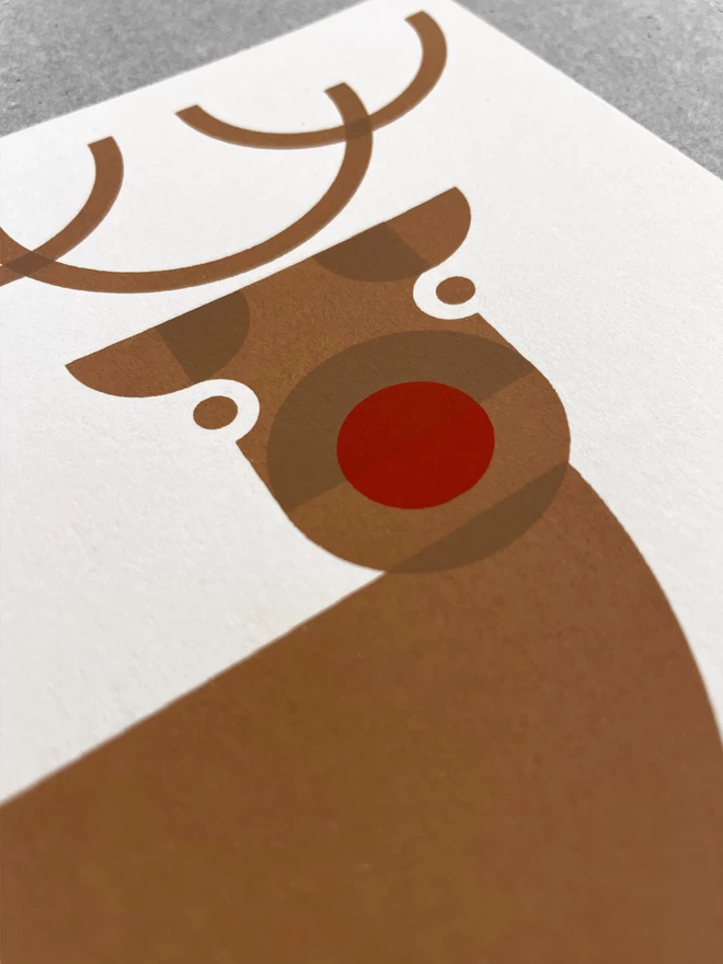 Close up of a Cheeky reindeer handprinted christmas card, Screenprinted in browns and red. Showing the overlapping printed layers of ink.