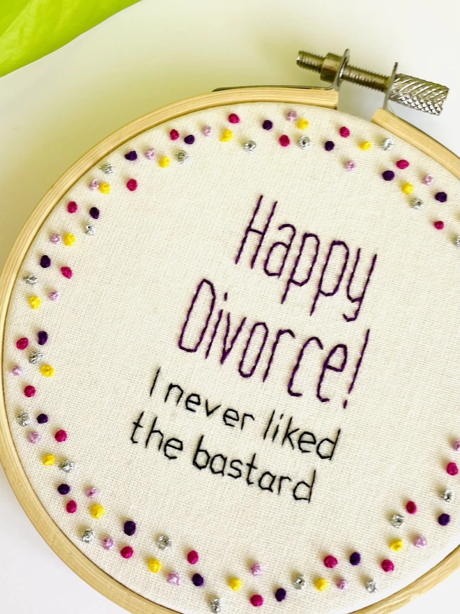 Hand embroidered wall hanging that reads Happy Divorce I never liked the bastard surrounded by multi-coloured french knots.