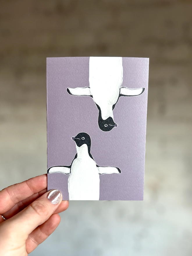 a purple greetings card featuring two illustrations of a penguin