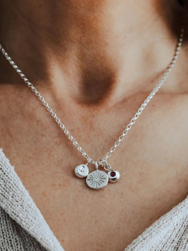 A woman wearing the Silver Darling Heart Pebble Necklace with two charms