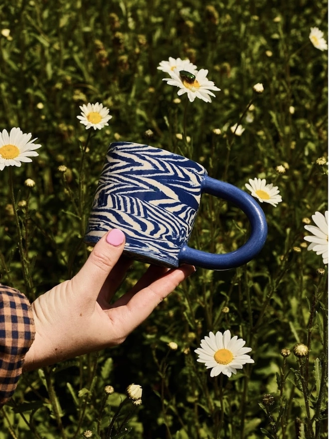 Herringbone Chunky Mug, a colourful mug held above a grassy backdrop. 