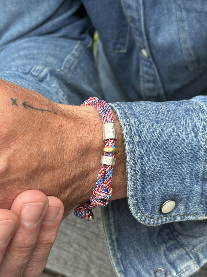 men's personalised drift paracord bracelet. a close up of a man's arm in a denim shirt wearing a red and blue paracord bracelet.
