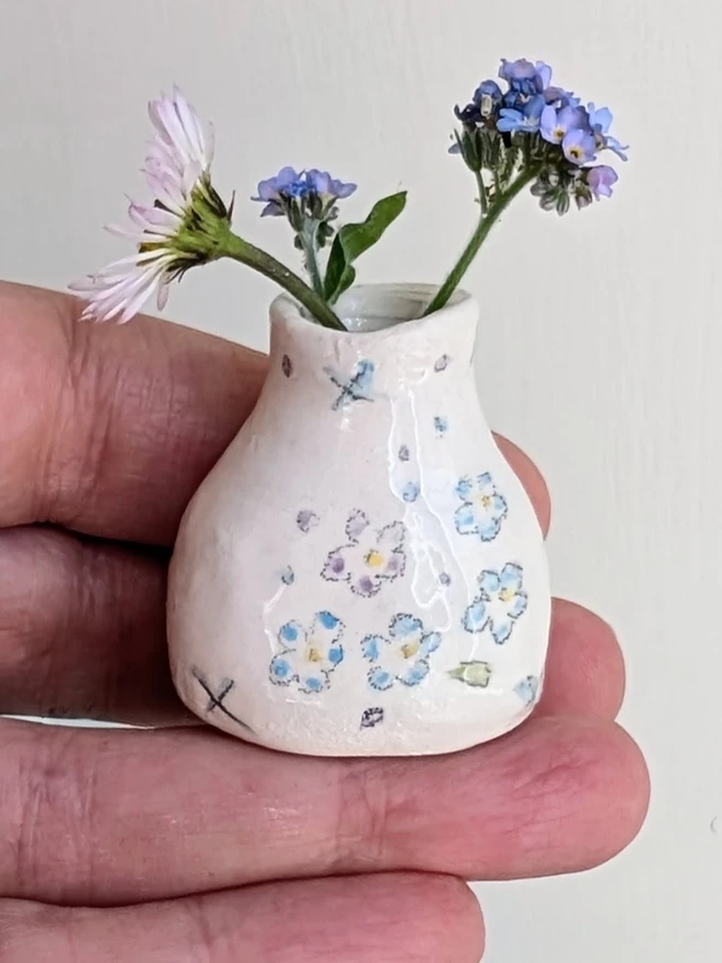 forget me not miniature vase held in a hand with daisy and forget me not flowers in and hand painted illustration