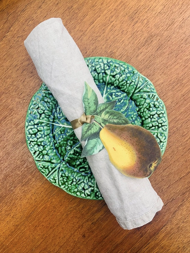 A place setting with cabbageware plate and linen napkin tied with a handcut fabric pear napkin ring