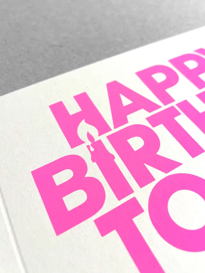 close up of neon pink ink printed on white recycled card, showing the candle created int he negative space of the Happy Birthday words.