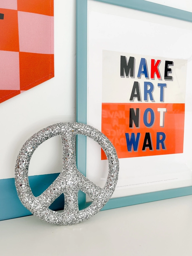 Silver peace sign on a shelf next to an art print saying make art not war