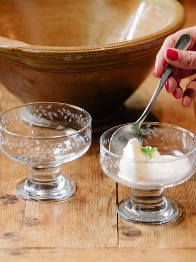 Two clear glass dessert bowls with an etched leaf pattern filled with ice cream and set on a rustic wooden table.