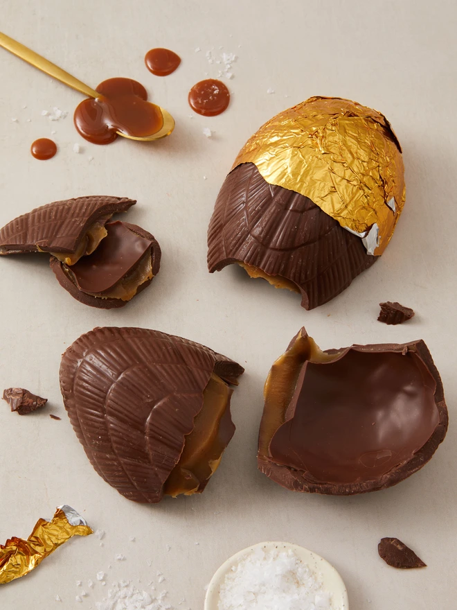 salted caramel milk chocolate easter egg. a chocolate egg photographed partially unwrapped from gold foil with salted caramel droplets.