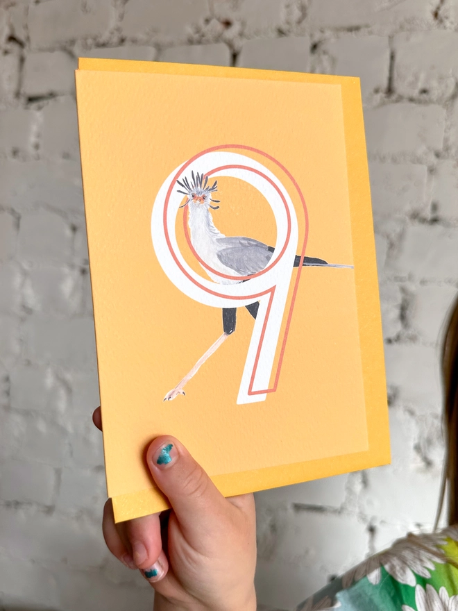 Bright yellow card with an illustration of a secretary bird and a big white number 9, with a yellow envelope