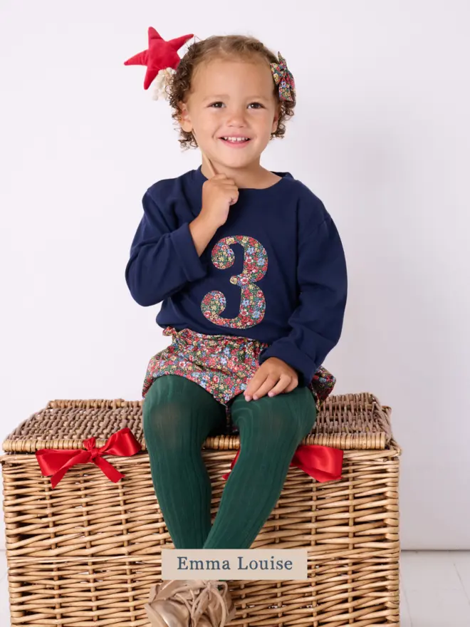 a 3 year old girl wearing a navy birthday t-shirt with a number 3 cut from liberty floral print on the front