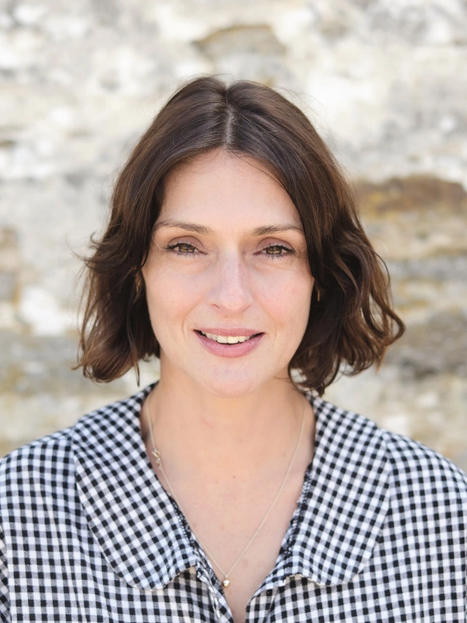 Woman with short brown hair and gingham blouse smiling a camera