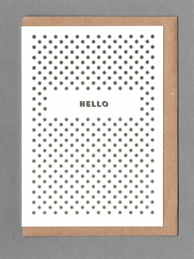 White card with black stars and black text reading 'Hello' with a brown envelope behind it