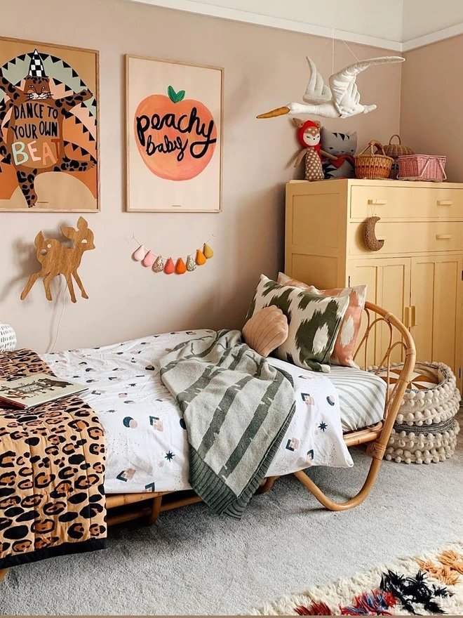 An image of a bright and colourful kids room with the birch forest baby blanket shown draped on a single bed.