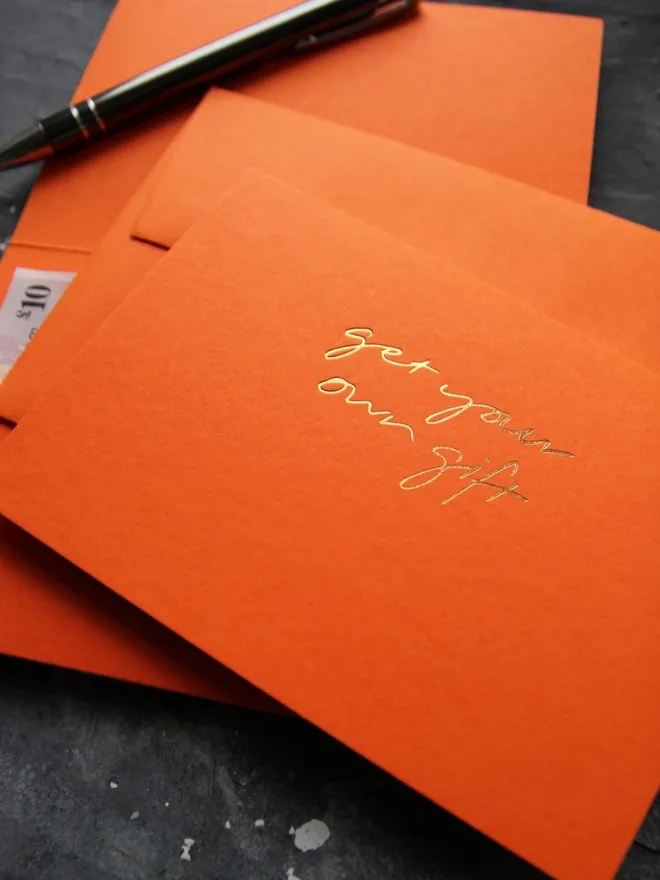 Hand foiled cash card or money wallet in a mandarin colour handfoiled in shiny golf foil text which says ‘get your own gift’.