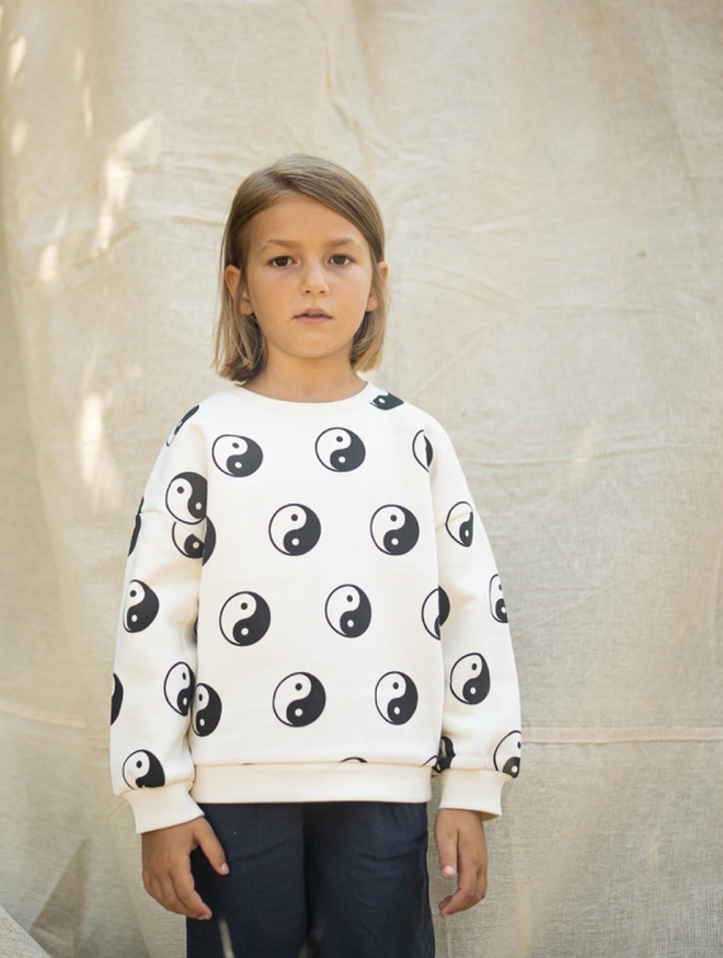 Child wearing the Another Fox Yin Yang Kids Sweatshirt standing in front of a white cloth. 