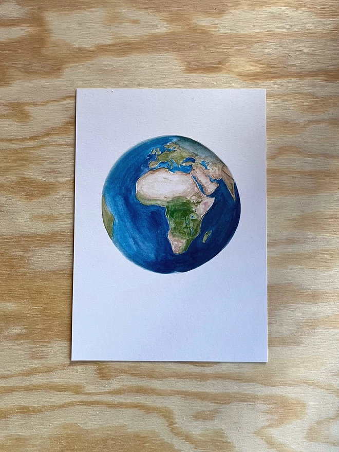 A painted illustration of Earth on a white background, sat on a sheet of wood