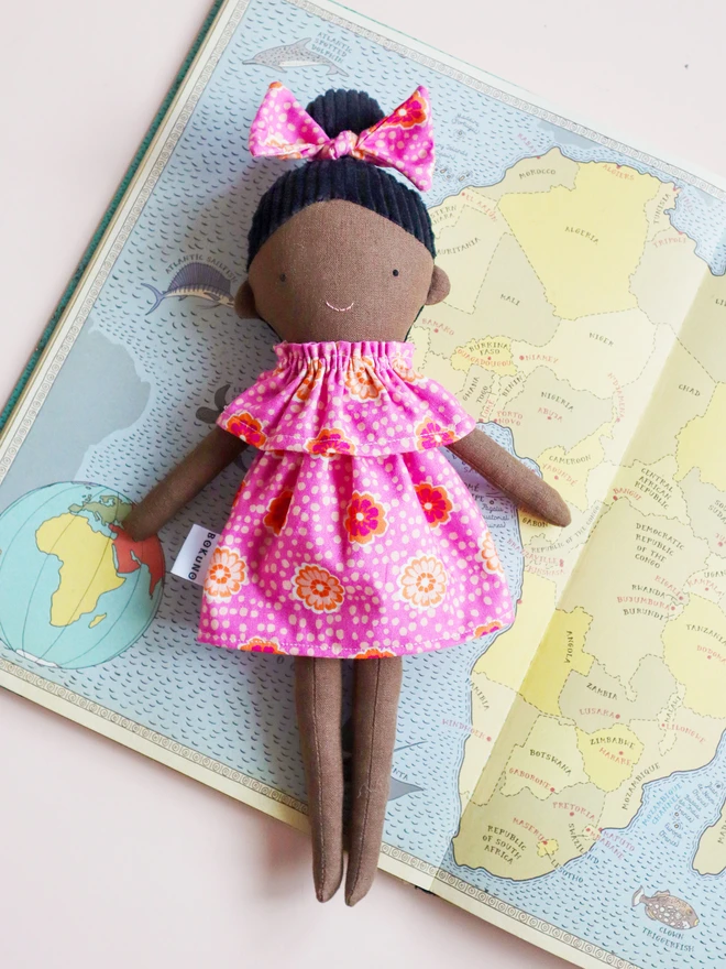 African-inspired handmade cloth doll with deep brown fabric skin, wearing a pink floral dress and matching bow