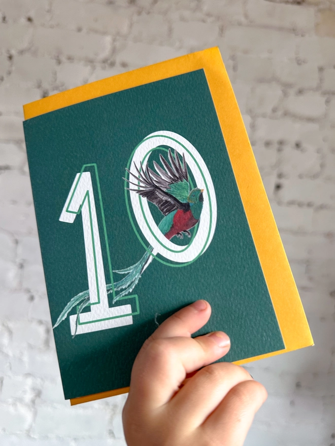 Deep green card featuring a big white number 10 and an illustration of a quetzal bird alongside a yellow envelope
