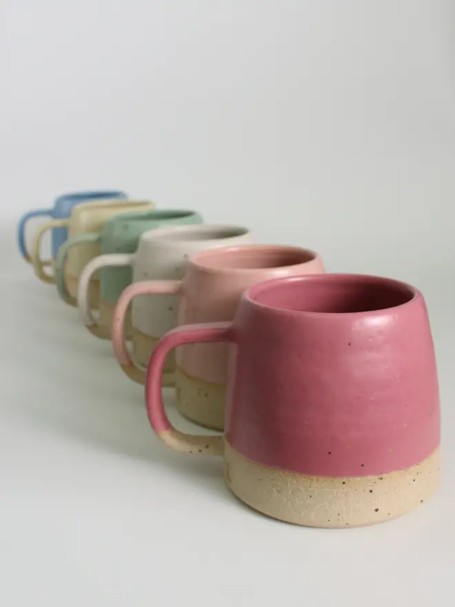Line-up of our stoneware ceramic mug collection. From back to front: cornflower blue, pale yellow, mint green, off-white, pale pink and fuchsia.