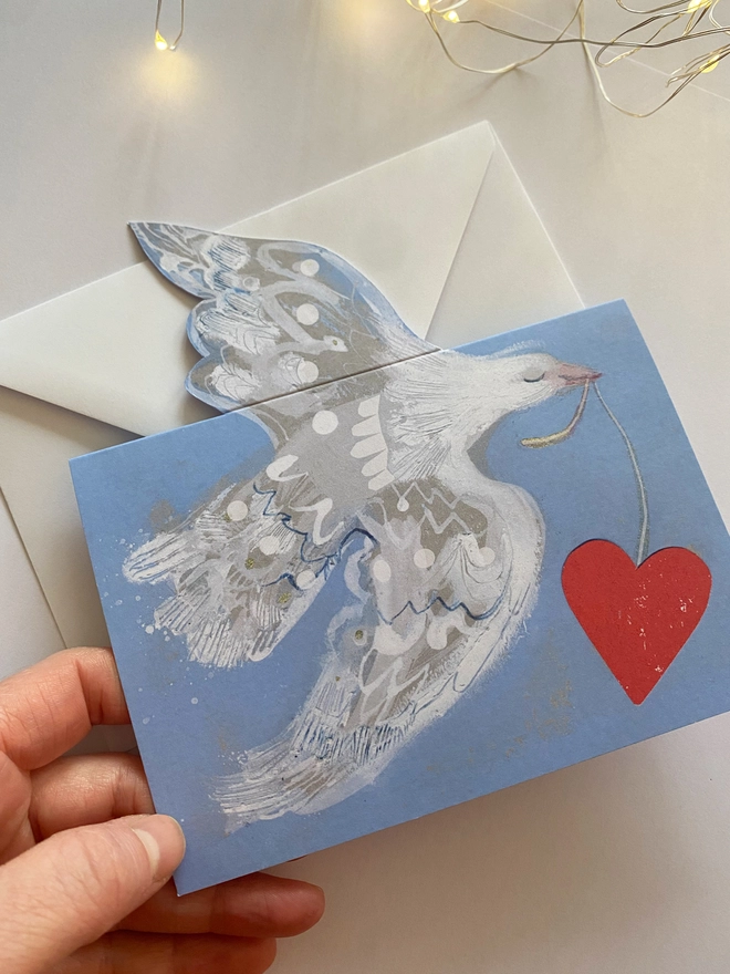 Esther Kent greetings card showing white flying dove in a light blue background, carrying a vibrant red heart on a string