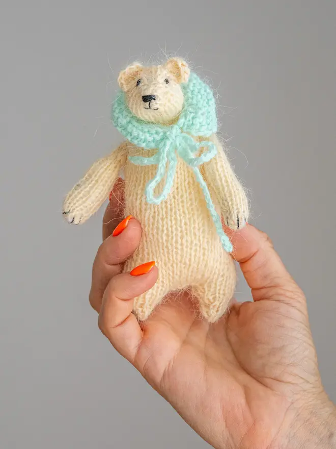 Ottilie The Bear Cashmere Figure , a cashmere bear held by a person against a grey backdrop. 