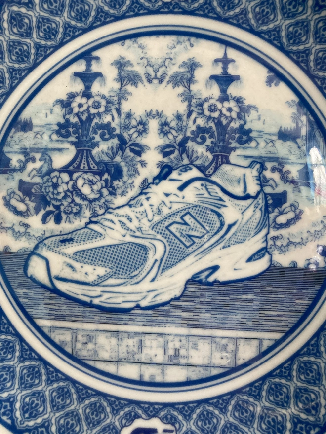 detail of plate showing the New Balance logo. The plate is blue and white in a Delft style featuring an illustration of a New Balance trainer in the centre