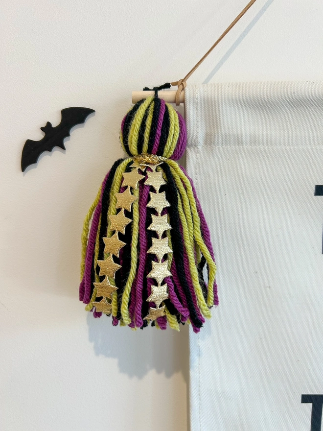 Purple, green and black tassels on a halloween banner with gold star detail. Black bat decoration