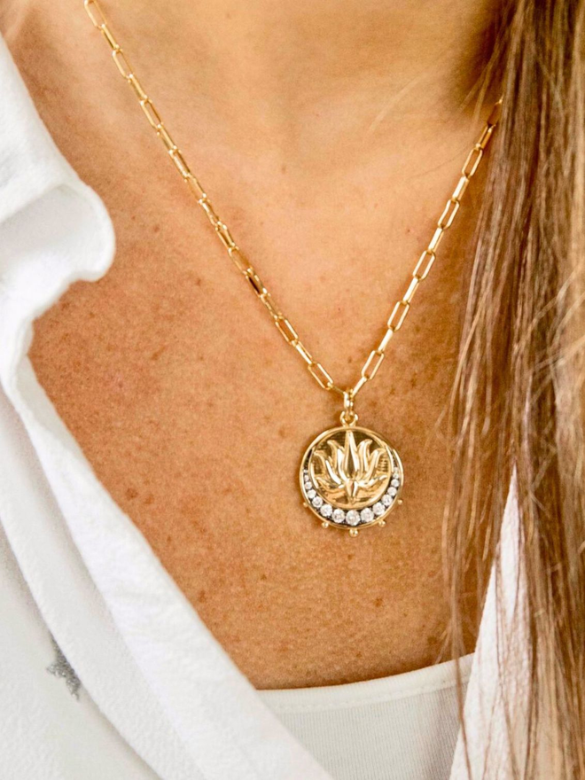 Gold and crystal lotus moon medallion charm hanging from gold paperclip chain necklace on women's neck