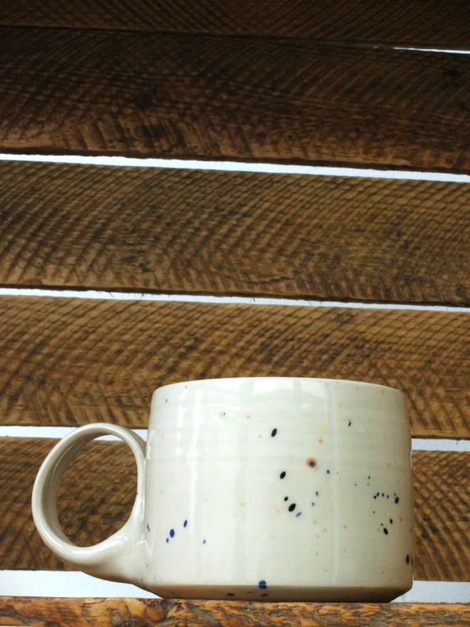 Small creamy white terrazzo cups with black, blue, and yellow splatters and glossy glaze
