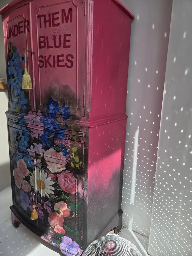 Side view of painted vintage wooden cabinet with pink, blue and floral decoration