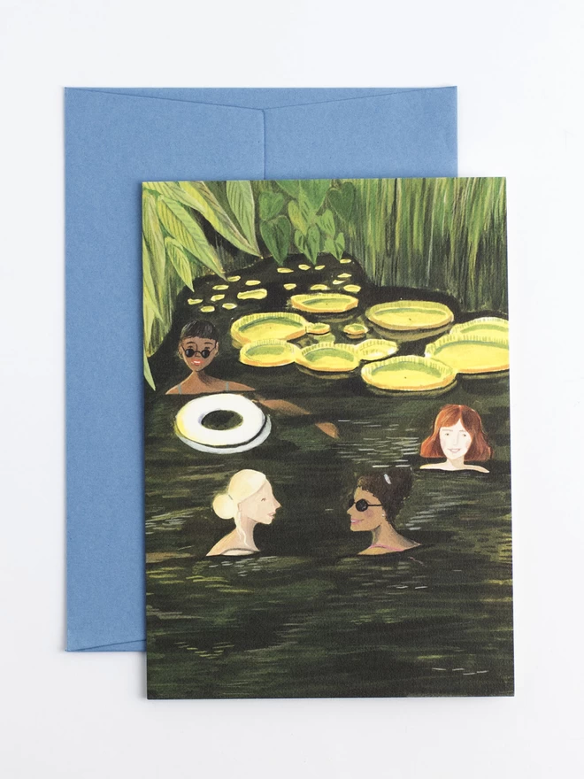 A greeting card featuring four women swimming happily in a green pond, they are surrounded by lush grass and vibrant yellow lily pads. 