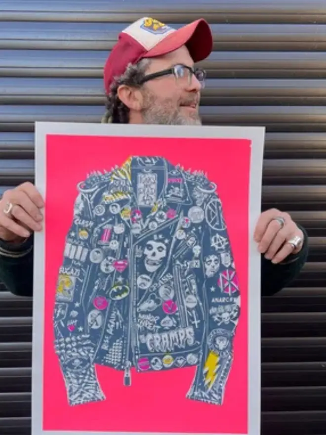 A punk leather jacket decorated with music band patches against a neon pink background, being held. 