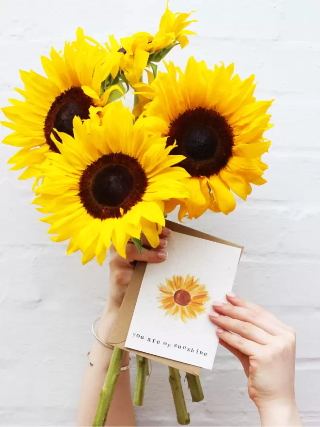 Hands holding bunch of sunflowers and 'You Are My Sunshine' Card