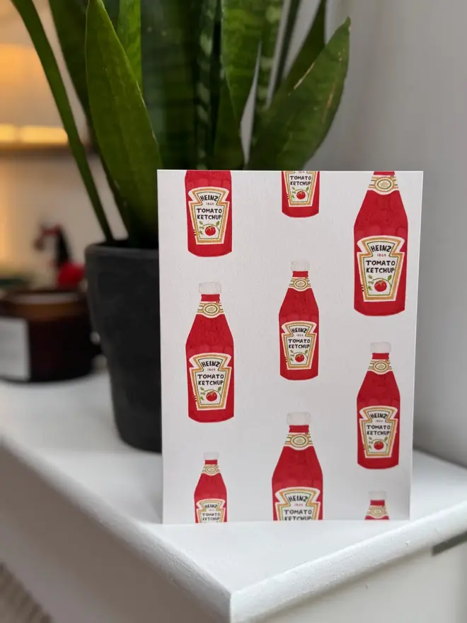 tomato ketchup bottles illustrated card. card photographed on mantelpiece with houseplant in the background.