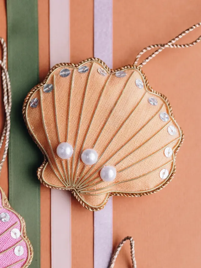 embroidered linen shell decoration. peach shell decoration photographed against stripy fabric background.