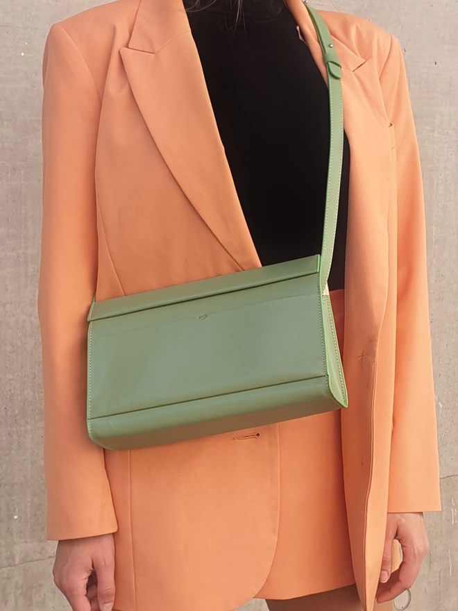 Sea Green Shoulder Bag readjusted to crossbody length worn on front of model. The model is of paler complexion wearing a peace blazer and short length skirt. There is a black blouse under the blazer.