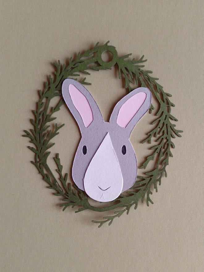 Black Bunny Easter Tree Decoration. Pale grey bunny face with white nose patch, black eyes and pale pink ears inside olive green foliage wreath oval