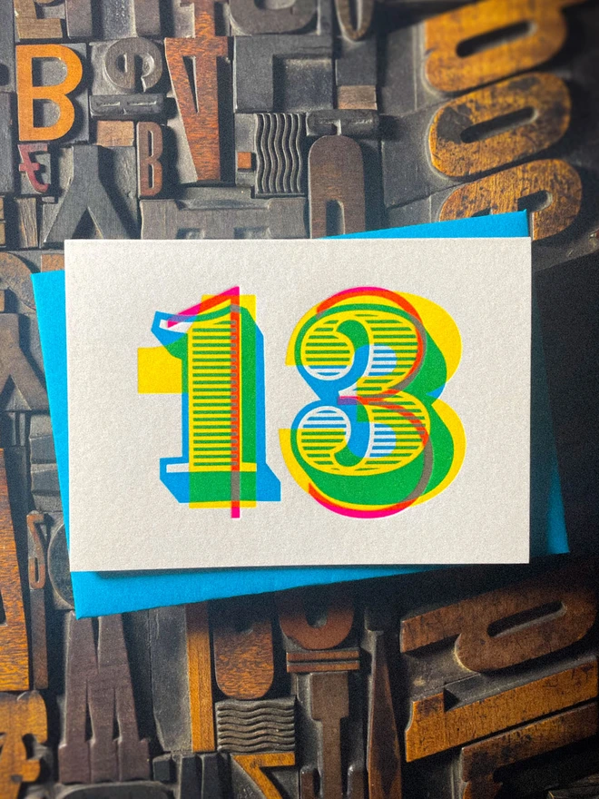 Handmade 13th birthday card paired with a bright blue GF Smith Colorplan envelope. The contemporary number 13 design is letterpress printed in overlapping cyan, magenta and yellow inks on premium Pristine White card.
