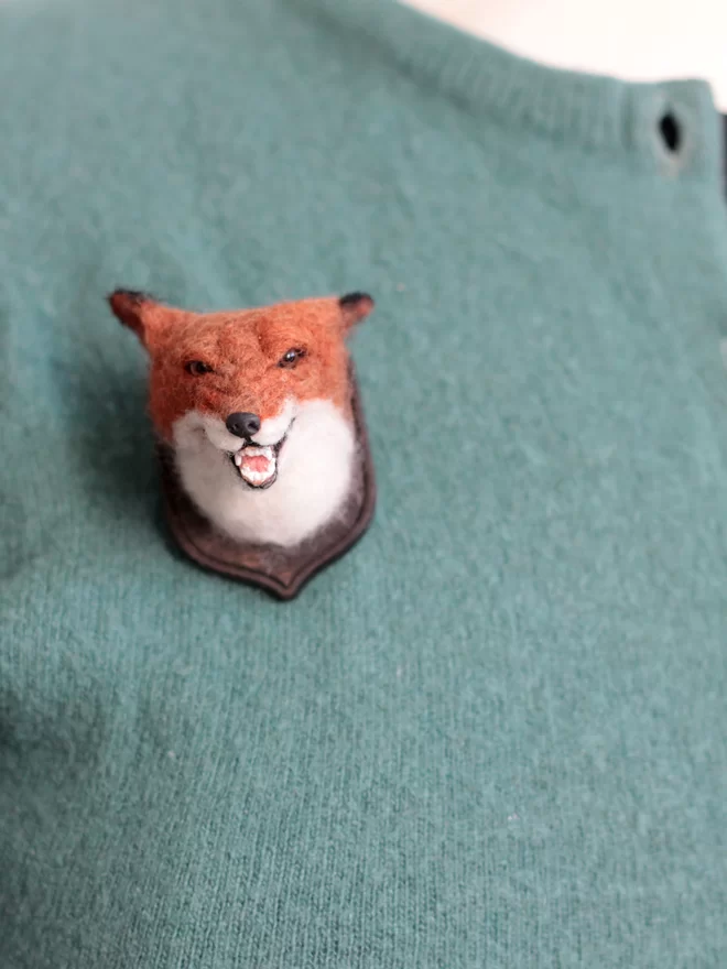 A miniature snarling fox head on a green cardigan