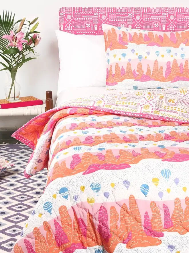Fairy Chimney Quilt, a pink and yellow quilt sitting on a bed in a bedroom. 