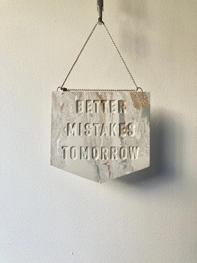 'Better Mistakes Tomorrow' Banner, a clay banner hanging against a plain backdrop.