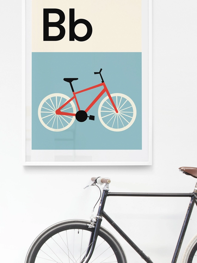 illustrated bike wall print hanging on a white wall with a real bike propped up in the foreground