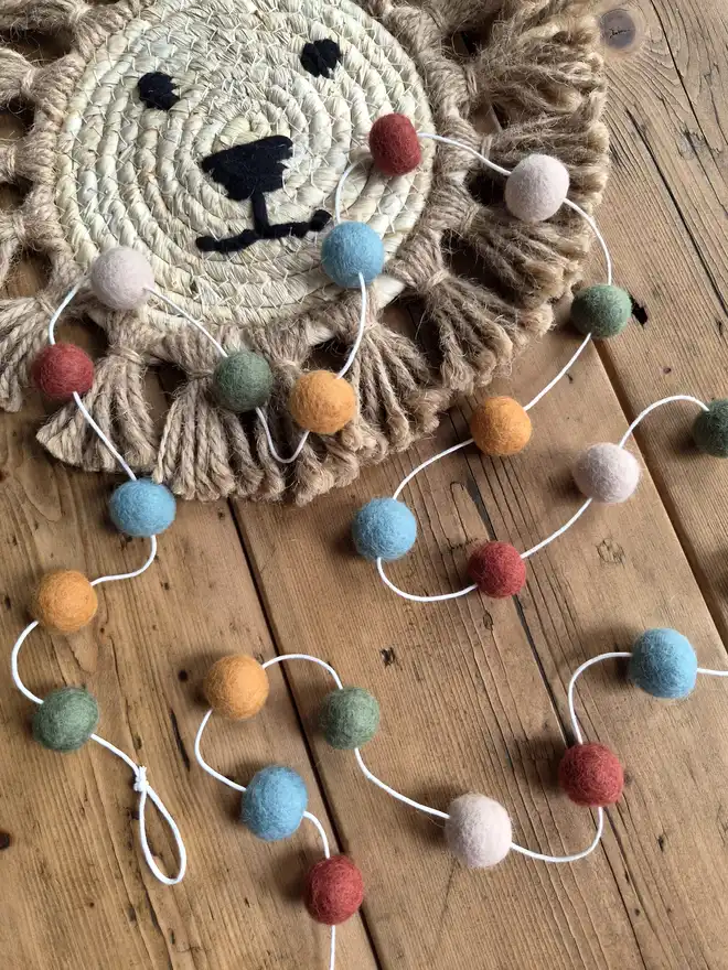 Pom pom garland in jungle colours laid on a wooden table.