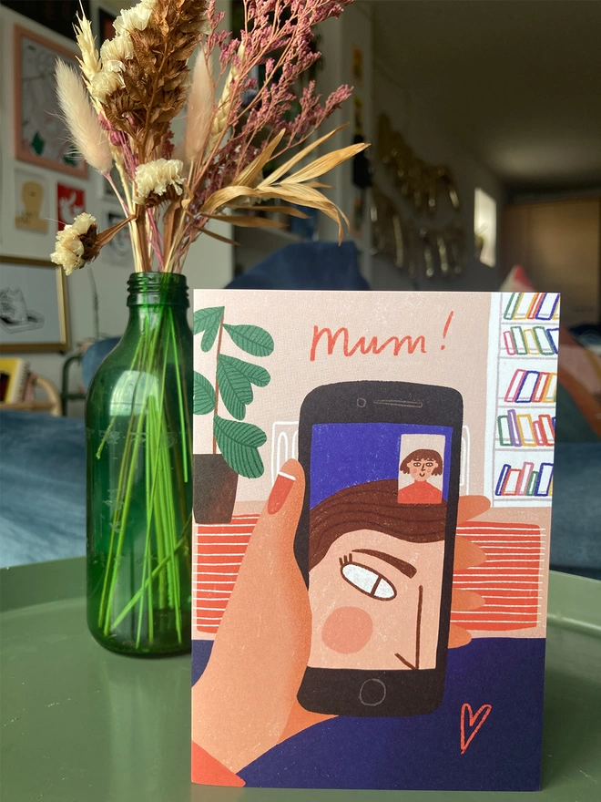 Greetings card featuring an illustration of a mum struggling to FaceTime, placed on a table with flowers in the background