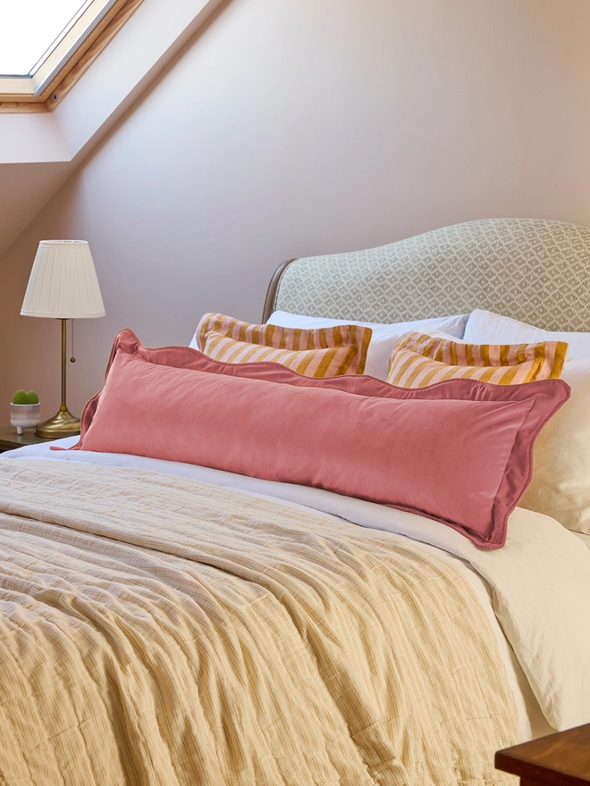 Handmade scalloped coral velvet bolster cushion 130cm with feather pad paired with stripe linen cushions on bed, Kika Bespoke